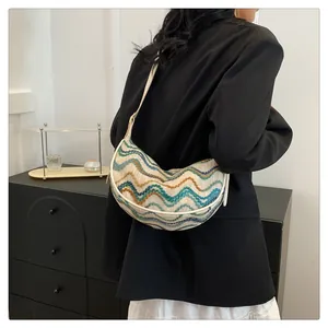 Close-up of woven crescent bag with colorful wave patterns and white leather shoulder strap