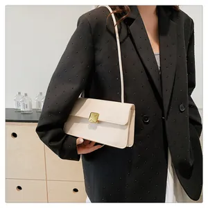 Sac bandoulière blanc crème chic avec boucle dorée porté sur un blazer noir élégant