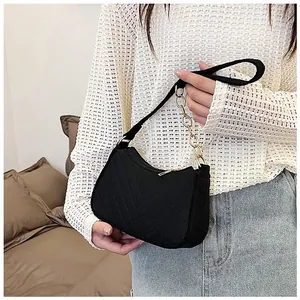 Close-up of black quilted felt underarm bag with gold chain and woven strap on model