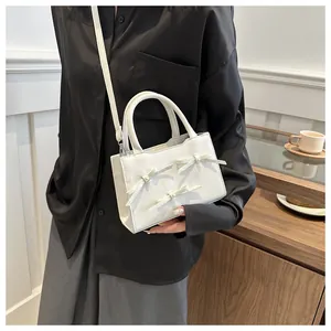 Close-up of white crossbody bag with decorative bow details and elegant pearl centers