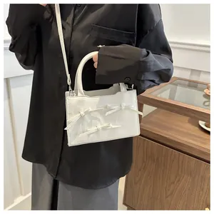 Detailed view of white crossbody bag with pearl bow accents on elegant black shirt