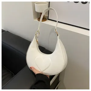 Detailansicht der Herz-Prägung auf der weißen Halbmondtasche mit goldenen Metallelementen
