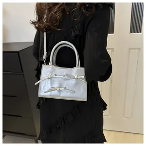 Silver bow-accented handbag with metallic texture worn by a model in a black dress