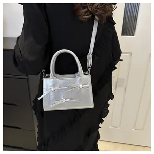 Silver bow shoulder bag with glossy finish and top handle shown on a model