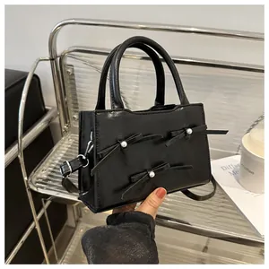 Detail of black crossbody bag featuring pearl bows on a glossy faux leather finish