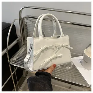 Detail of white leather handbag featuring pearl-studded bows and a metallic side hook