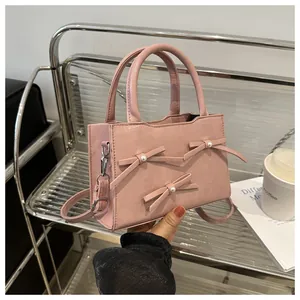 Detail of pink pearl bow handbag featuring glossy leather texture and silver metal clips