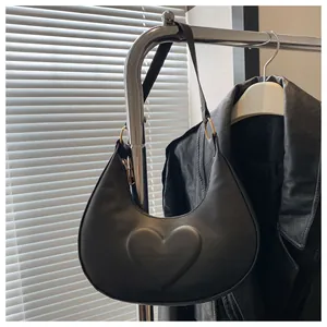 Detail der schwarzen Ledertasche in Halbmondform mit Herzprägung und Goldringen