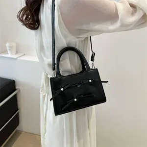 Elegant black PU leather handbag with pearl bows on a white minimalist background
