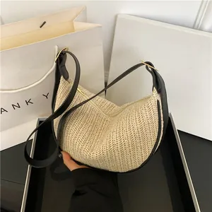Beige woven straw shoulder bag with black leather trim and adjustable strap in a gift box