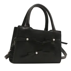 Elegant black structured handbag with pearl bow details and adjustable shoulder strap