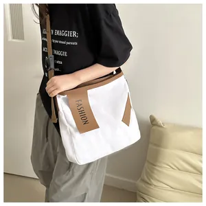 Dettaglio di una borsa a tracolla in tela bianca con bordo marrone e targhetta FASHION