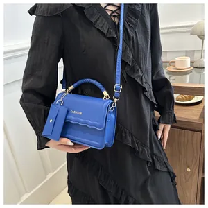 Sac bandoulière bleu avec poignée tressée et petit porte-monnaie porté par un mannequin