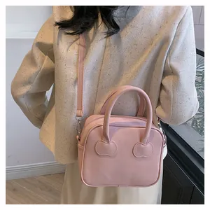 Rear view of a minimalist pink crossbody bag on model with adjustable strap and heart stitching