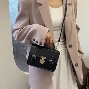 Classic black leather satchel with gold buckle and top handle worn over a lilac blazer