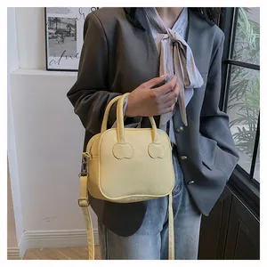 Detail view of light yellow square bag with cherry emblem and adjustable shoulder strap