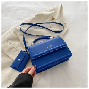 Détail du sac à main bleu avec poignée tressée et lettrage doré sur le rabat ondulé