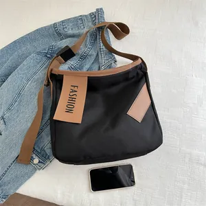 Borsa tote in tela nera con tracolla marrone e toppa con lettere su sfondo denim