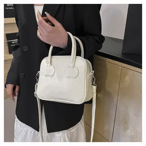 White minimalist square handbag with apple-shaped stitching details and long strap