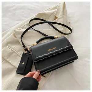 Détail du sac bandoulière noir à bords ondulés avec texte doré et mini pochette monnaie