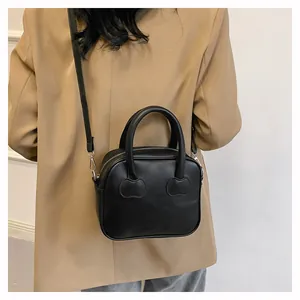 Detail of black handbag with heart-shaped stitching shown on shoulder with beige blazer