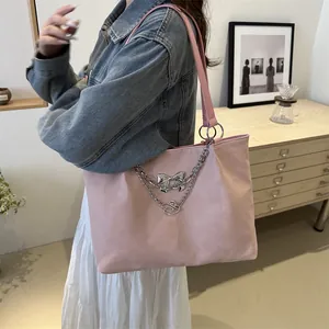 Pink shoulder tote bag with silver metal bow and chain detail in a warm lifestyle setting