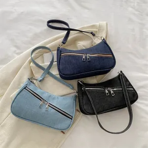 Borse a spalla in denim nero e blu con doppia cerniera su sfondo beige neutro
