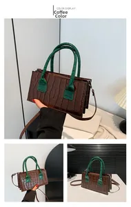Dettaglio di una borsa marrone con motivo a coccodrillo, manici verdi e piccola forma quadrata