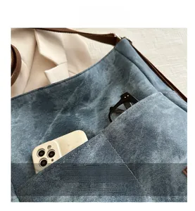 Detail of blue denim crossbody bag featuring two front pockets for phone and glasses storage