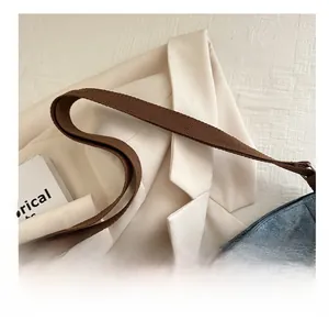 Detail showing the adjustable brown fabric shoulder strap on the denim blue tote bag