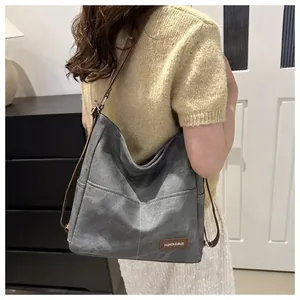Detail of grey denim tote bag showing brown leather logo and reinforced side stitching