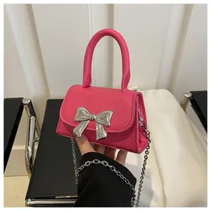 Detail of pink faux leather handbag featuring a silver metal bow and chain strap