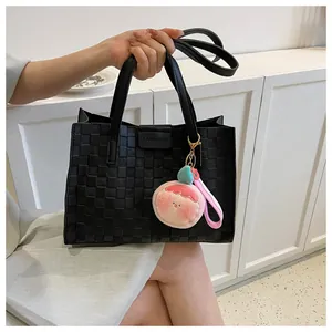 Detail of black woven checkerboard tote bag with pink plush peach charm accessory