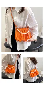 Detail of orange ruched cloud bag featuring pearl handle and leather shoulder strap