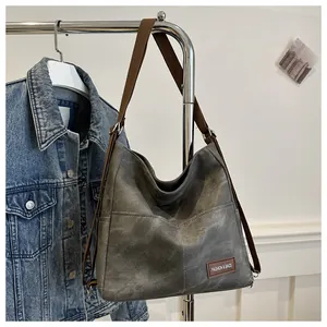Detail view of denim canvas bag with leather logo tag and durable brown shoulder strap