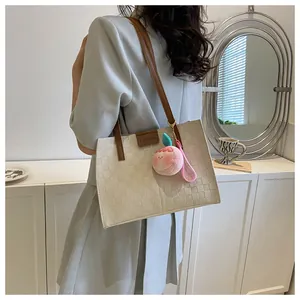 Detail of off-white woven tote bag featuring a leather FASHION label and peach plush charm
