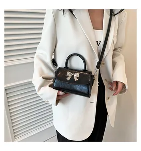 Detail of glossy black handbag featuring a silver metal bow buckle and elegant top handle