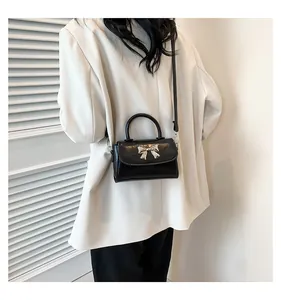 Close-up of black glossy crossbody bag with silver bow ornament and slim shoulder strap