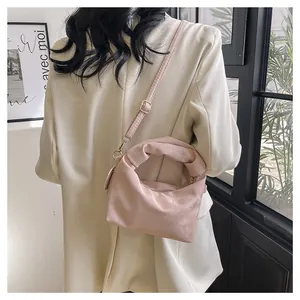 Pink pleated handbag with knotted handle shown from a side perspective on a model