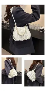 Detail of white pleated cloud bag featuring pearl handle and braided rope shoulder strap