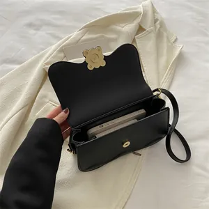 Sac sous le bras noir chic avec fermoir fleur dorée et rabat ondulé sur un blazer