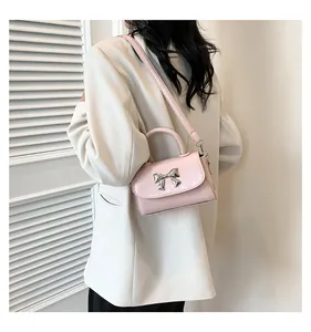 Pink crossbody bag with silver bow detail worn by model in white blazer outfit