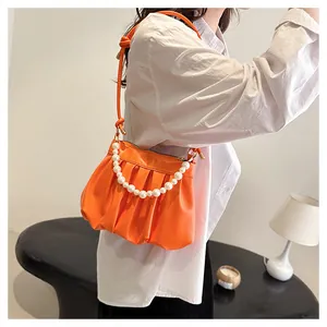Detail of orange ruched cloud bag featuring pearl chain strap and shoulder handle on model