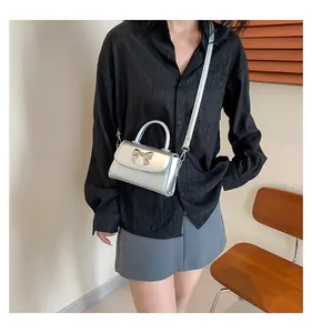 Detail view of a silver metallic crossbody bag with bow hardware on a fashion model