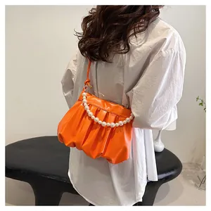 Detail of orange pleated cloud bag with white pearl handle and sleek leather texture