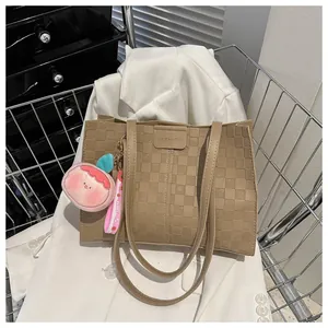 Detail of brown checkered tote bag with embossed logo and peach plush charm on white blazer