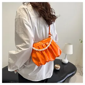 Detail shot of orange pleated cloud bag with pearl chain handle on a model shoulder