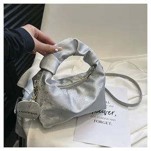Close-up of metallic silver pleated handbag featuring glitter texture and brand tag