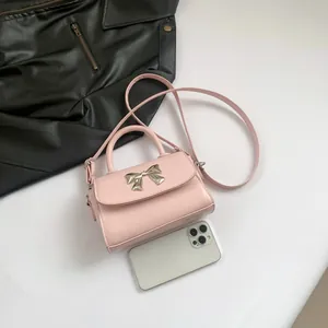 Pink mini square handbag with metal bow detail and smartphone for scale reference