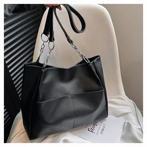 Detalle del bolso shopper negro con correas de cadena y cuero y costuras en bolsillos frontales